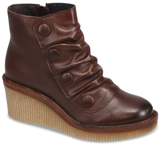A dark brown leather ankle boot with a side zipper, featuring four decorative buttons along the side and a ruched shaft on a tan, ridged wedge sole.