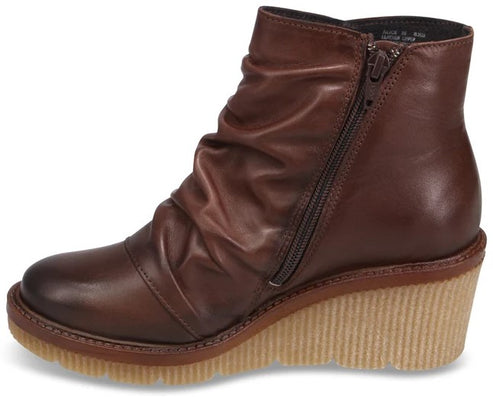 A brown leather ankle boot with a side zipper, a ruched upper, and a thick, ridged tan wedge sole.