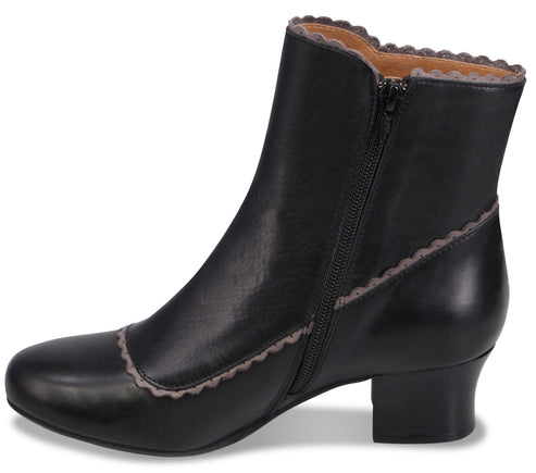 A black leather ankle boot with a low block heel, side zipper, and scalloped trim along the collar and toe seam.