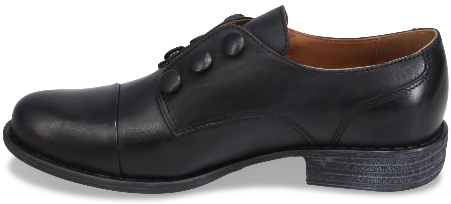 A black leather men's dress shoe with a cap toe, featuring a unique side button closure instead of laces, and a weathered grey-toned sole.