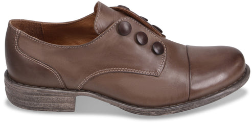 A side view of a brown leather cap-toe shoe with decorative side buttons and a distressed light brown rubber sole.