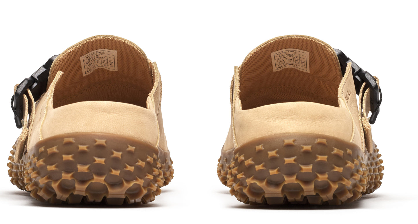 Back view of pair of closed-toe beige sandals with nubbed brown soles and black buckle.