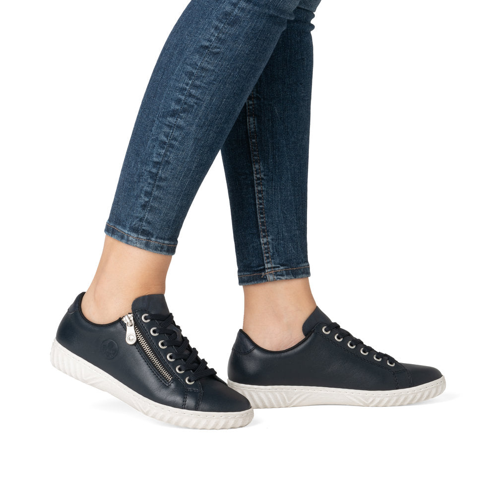 A person wears blue jeans and navy sneakers with white soles; one sneaker has a side zipper.