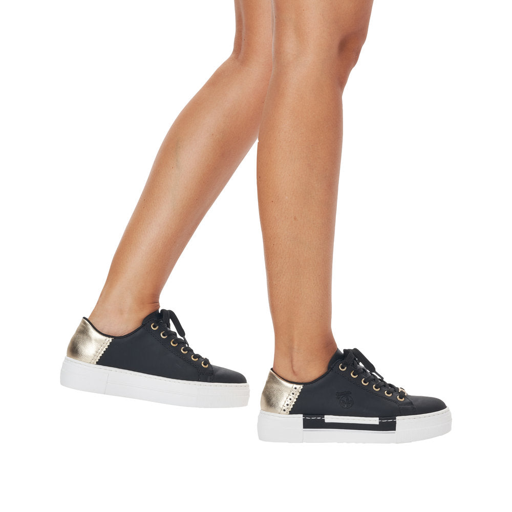 A pair of dark blue leather sneakers with gold heel detail and white soles are worn on feet.