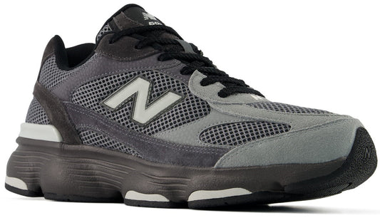 A New Balance 990v6 running shoe in a grey and black colorway featuring a mesh and suede upper, a prominent white N logo on the side, and a chunky, dark-toned midsole.