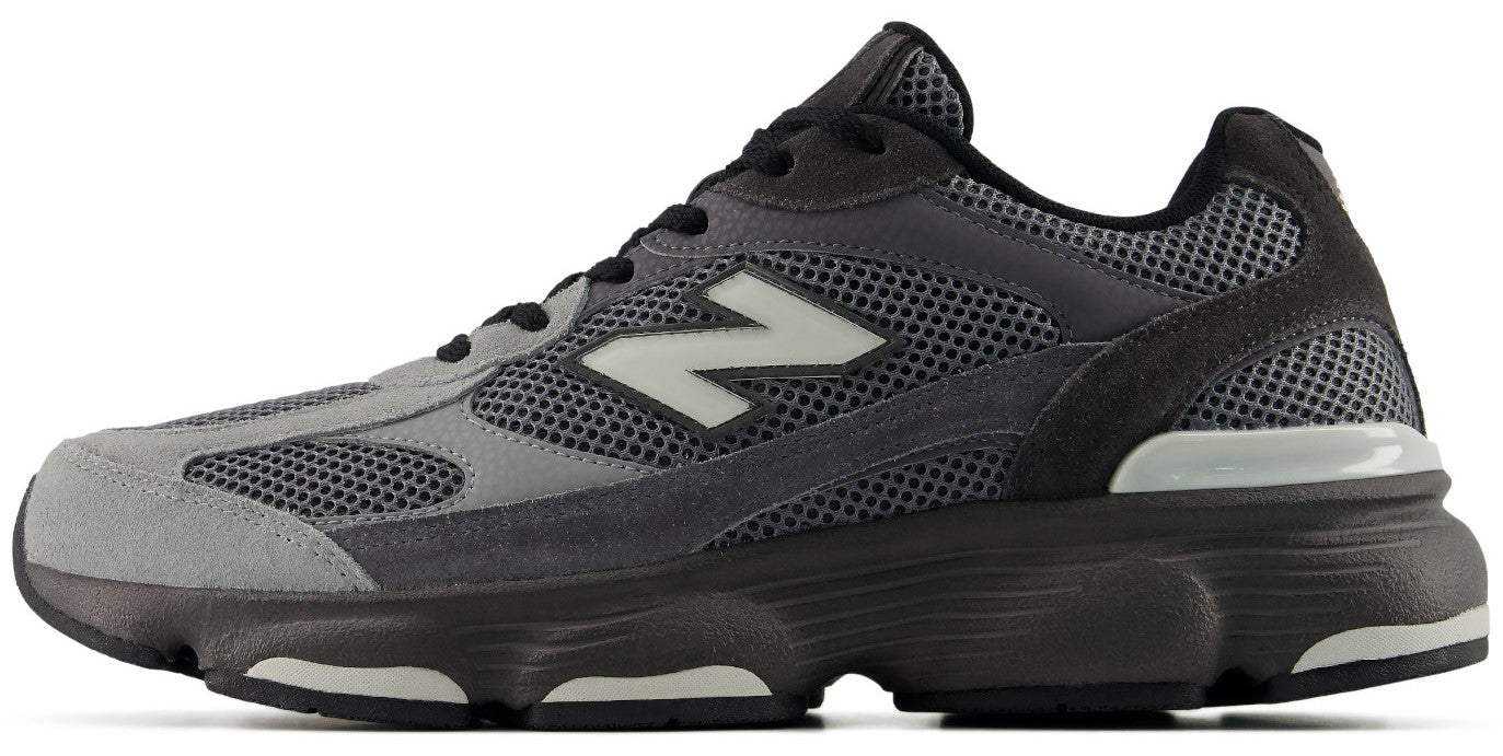A low-top running shoe featuring a mesh and suede upper in shades of grey and charcoal, with a prominent white 'N' logo on the side and a chunky dark grey sole.