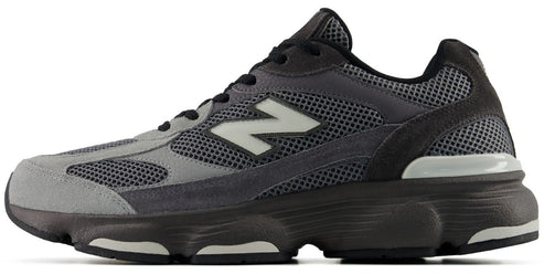 A low-top running shoe featuring a mesh and suede upper in shades of grey and charcoal, with a prominent white 'N' logo on the side and a chunky dark grey sole.