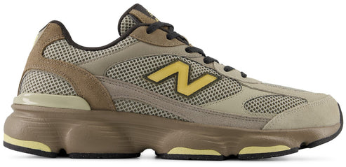A low-top athletic sneaker in shades of olive, tan, and dark brown, featuring a mesh and suede upper, a prominent yellow N logo on the side, dark brown laces, and a chunky brown midsole with pale yellow accents on a black rubber outsole.