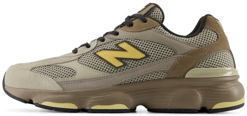 A low-top athletic sneaker in muted earthy tones, featuring a tan mesh base with light brown suede overlays, a yellow 'N' logo on the side panel, and a chunky brown midsole with yellow accents.