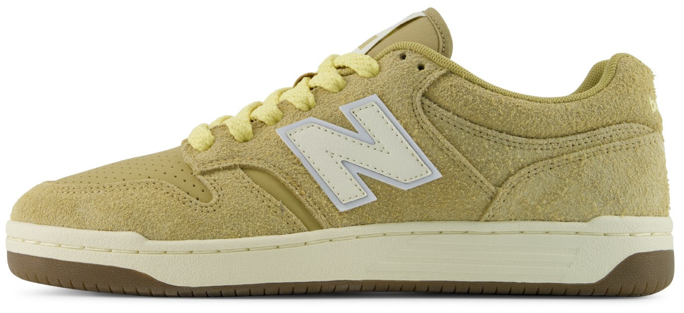 A low-top suede sneaker in a muted olive-yellow color with a cream-colored N logo on the side, cream laces, a cream midsole, and a dark gum brown rubber outsole.