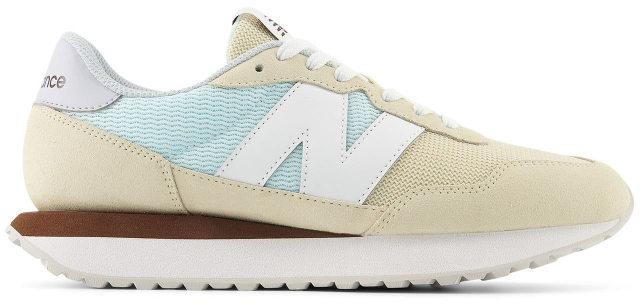 A sneaker with a beige suede upper, white laces, a white "N" logo, and a thick white sole.