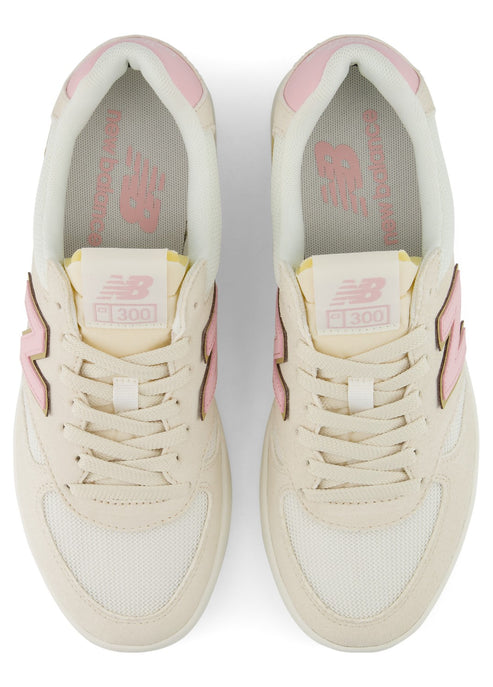 A pair of cream-colored New Balance 300 sneakers with light pink accents on the tongue, collar, and side branding, viewed from directly above.