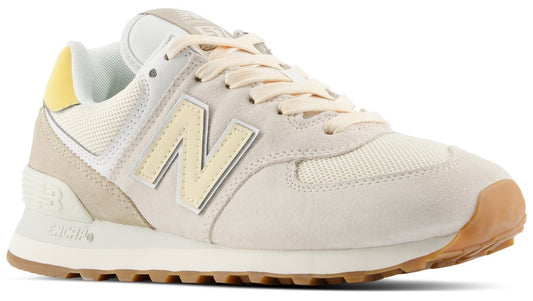 A New Balance 574 sneaker in cream and off-white suede and mesh with a yellow heel tab, a pale yellow N logo on the side, and a brown gum rubber outsole.
