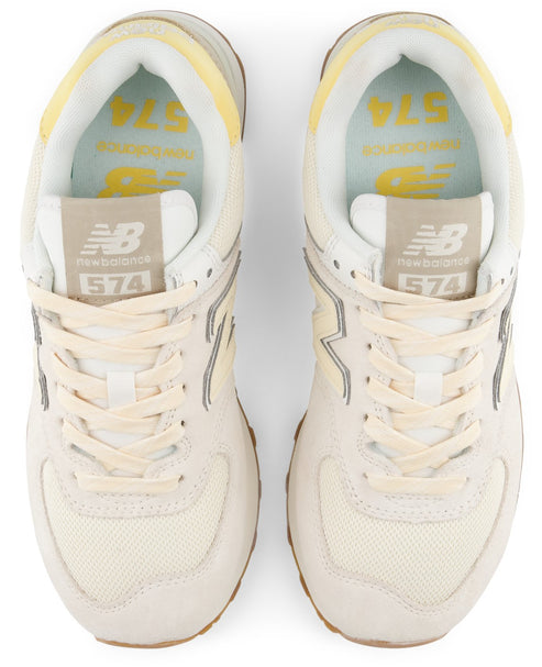 A pair of top-down view of cream-colored New Balance 574 athletic shoes featuring a mesh and suede upper, light yellow collar trim, and branded insoles with the number 574.