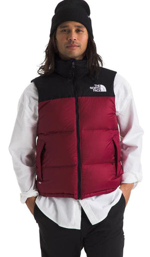 A man wearing a black beanie, black and red puffer vest, and white collared shirt.