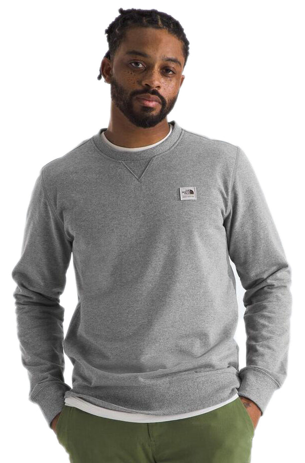 Man wearing a gray long-sleeve shirt with a small square logo and green pants.