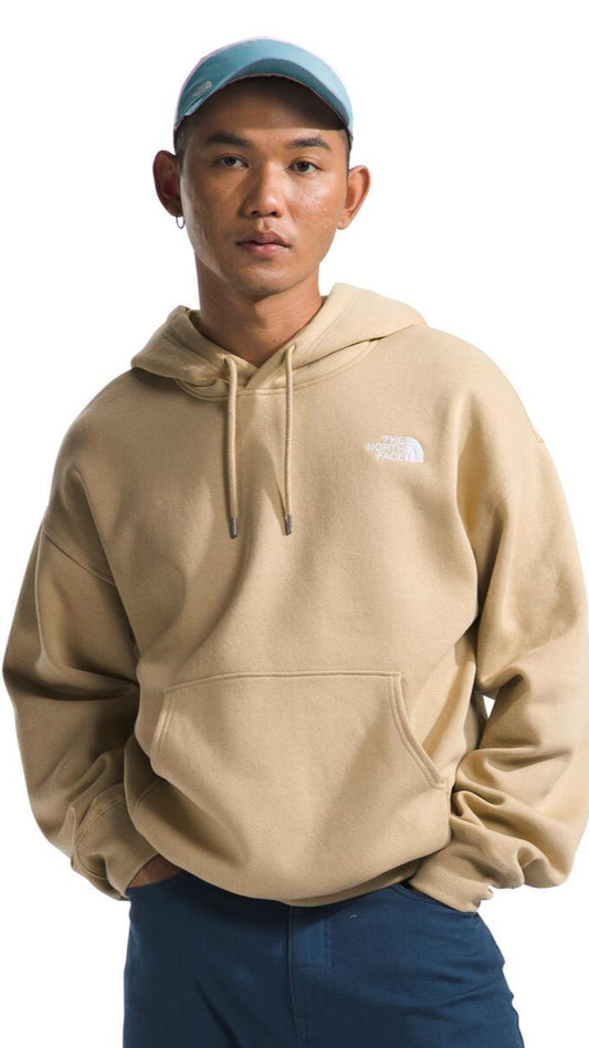 A person wearing a beige hoodie with a logo and a blue baseball cap.