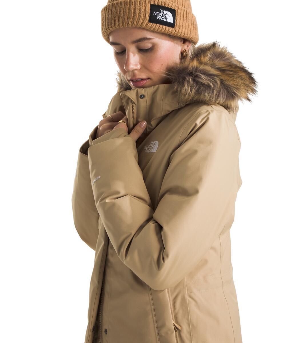 Woman wearing a tan beanie and winter coat with fur hood.