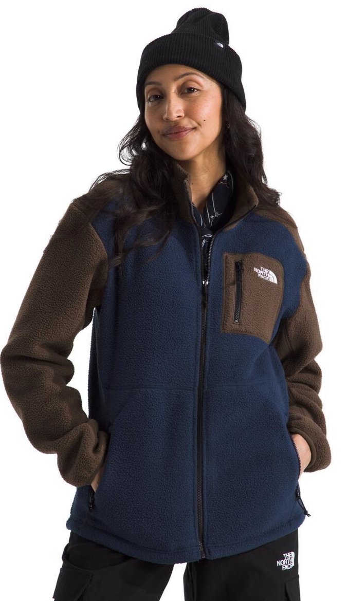 A woman wearing a beanie and a fleece jacket with brown sleeves and a navy blue body. The jacket has a zippered chest pocket with a brown border.