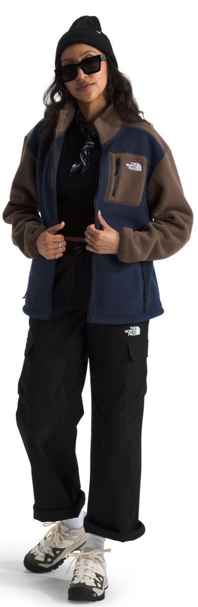 A person wearing a black beanie, sunglasses, a color-blocked fleece jacket, black pants and sneakers.