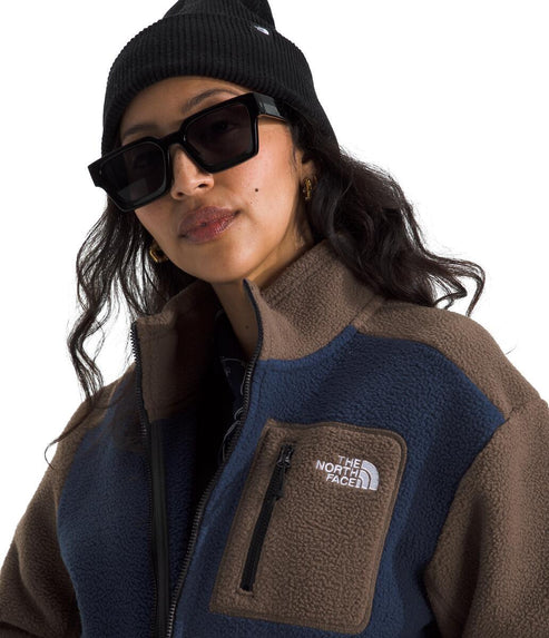 A woman wearing a black beanie and black sunglasses, modeling a navy and brown fleece jacket with a zipper pocket and The North Face logo.