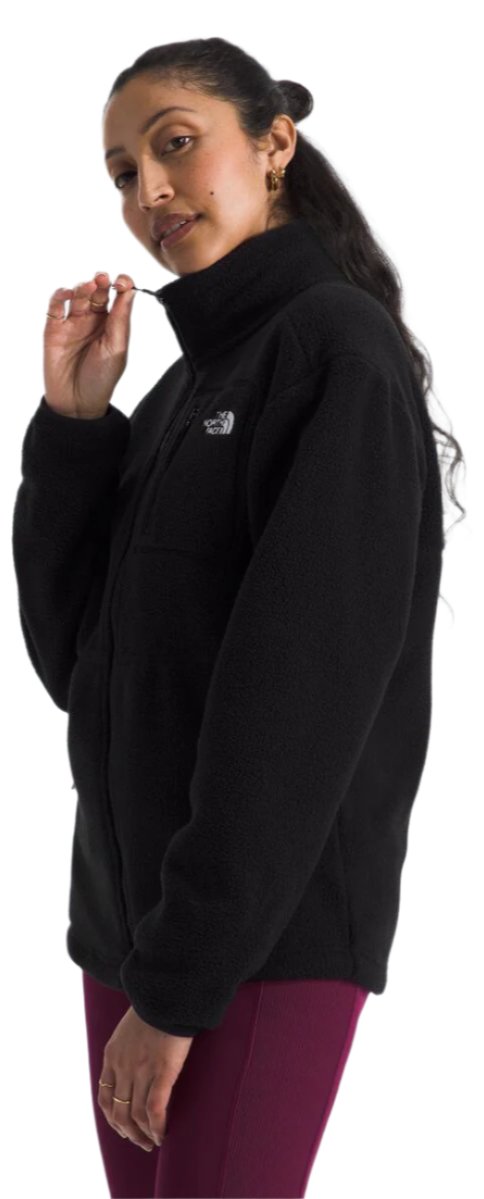 A person wearing a black fleece jacket with a high collar and a zipper, with burgundy pants.