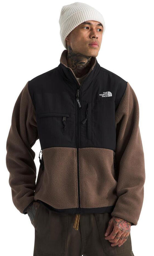 A person wearing a beige beanie and a black and brown fleece zip-up jacket with visible logo patch.