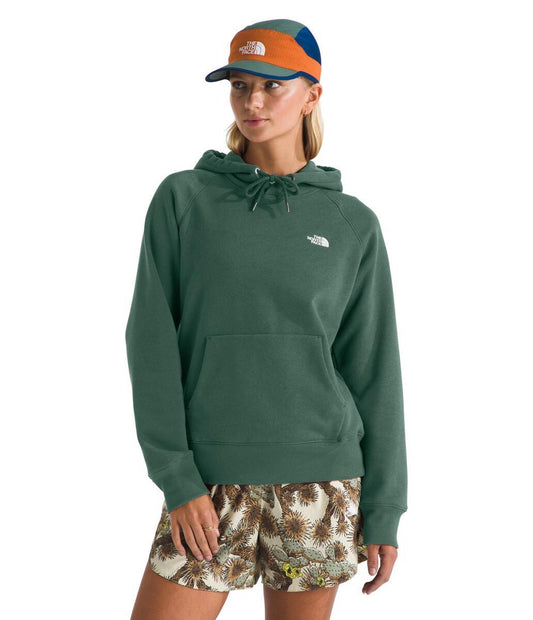 A woman in a green hoodie and floral shorts is wearing a multicolored cap.