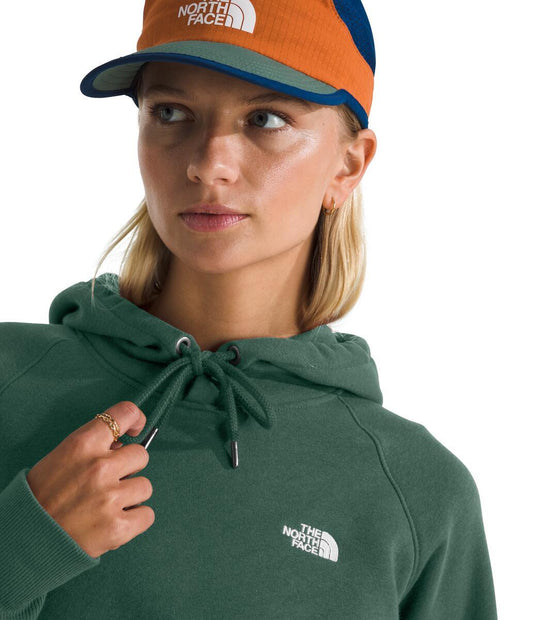 Person wearing a green hoodie with a white logo, and an orange and blue baseball cap.