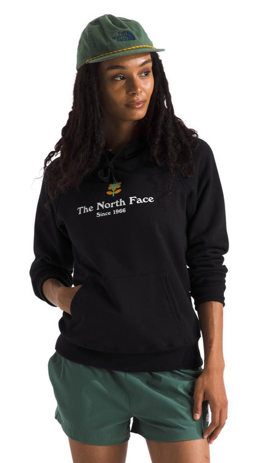 A person wearing a black hoodie with white text 'The North Face Since 1966', green shorts and cap.