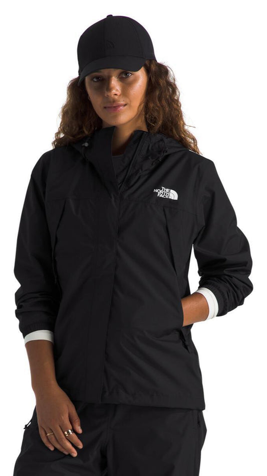 A woman wearing a black jacket and matching baseball cap, with her hand in the jacket pocket, showcasing a white cuff.