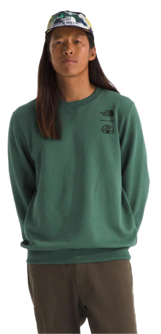 A person wearing a green long-sleeved shirt, brown pants, and a patterned hat.