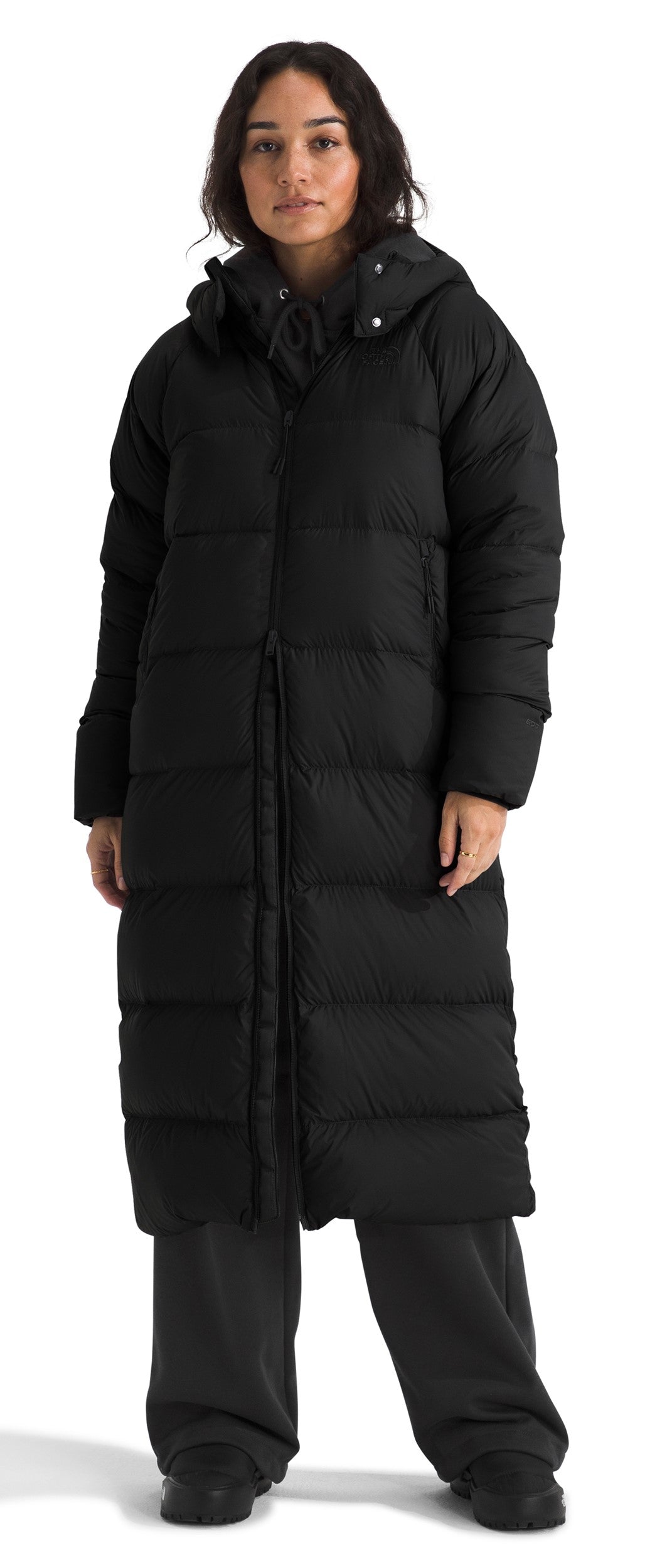 A person is wearing a long, black, hooded, padded coat and black pants.