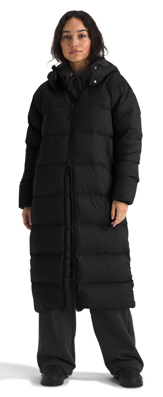 A person is wearing a long, black, hooded, padded coat and black pants.