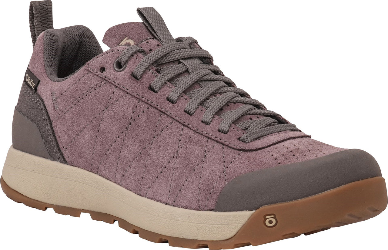 A mauve-colored suede athletic shoe with a lace-up front, cream-colored midsole, and brown rubber outsole, featuring decorative stitching across the upper and an O-shaped logo on the toe.