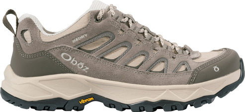 A low-top hiking shoe in shades of taupe and light brown, featuring mesh and suede panels, a thick, lugged Vibram sole, a lacing system, a heel pull tab, and the text Oboz printed on the side.