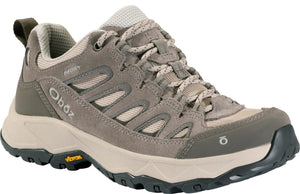 A low-top taupe-colored hiking shoe with suede and mesh upper, patterned laces, a thick beige midsole, a dark grey Vibram rubber outsole, and the Oboz logo on the side heel and front toe.