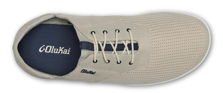 A tan colored slip-on sneaker with white laces and a navy-blue insole with 'OluKai' in white font.
