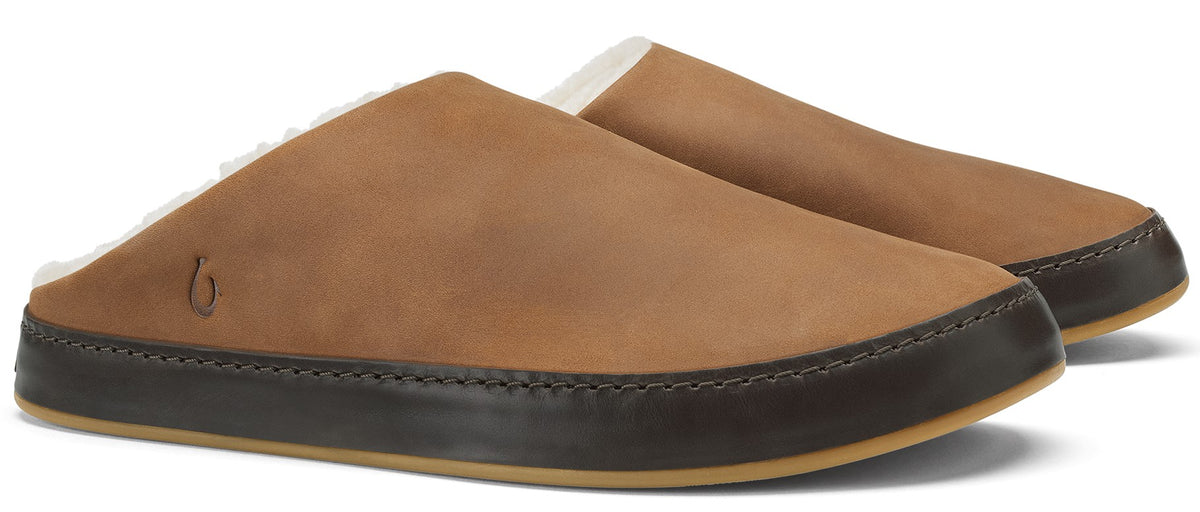 A pair of tan leather slip-on slippers with a dark brown leather mudguard and a light-colored shearling lining, featuring a small logo stamped on the side.