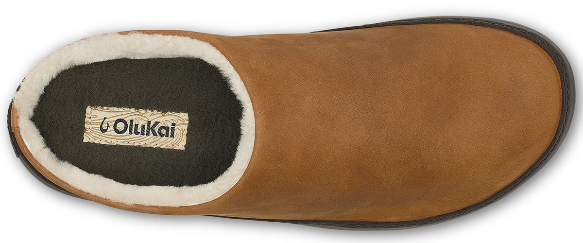 A top-down view of a tan leather slip-on mule lined with white faux fur, featuring an OluKai brand label on the black footbed.