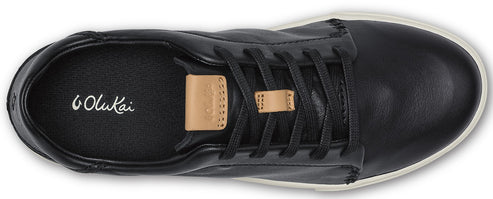 Overhead shot of a black leather sneaker with black laces and a tan leather lace tag, featuring white "OluKai" lettering inside.