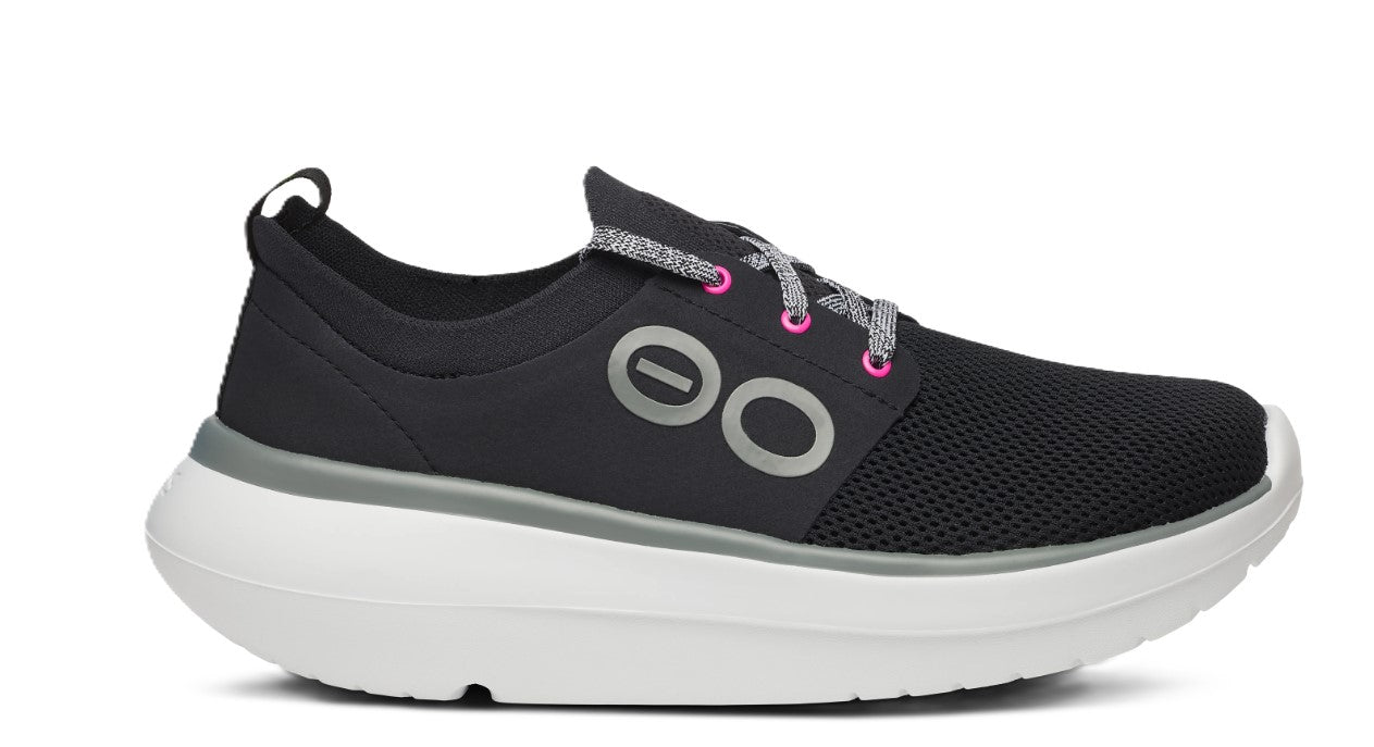 A black sneaker with gray and pink laces and a thick white sole.