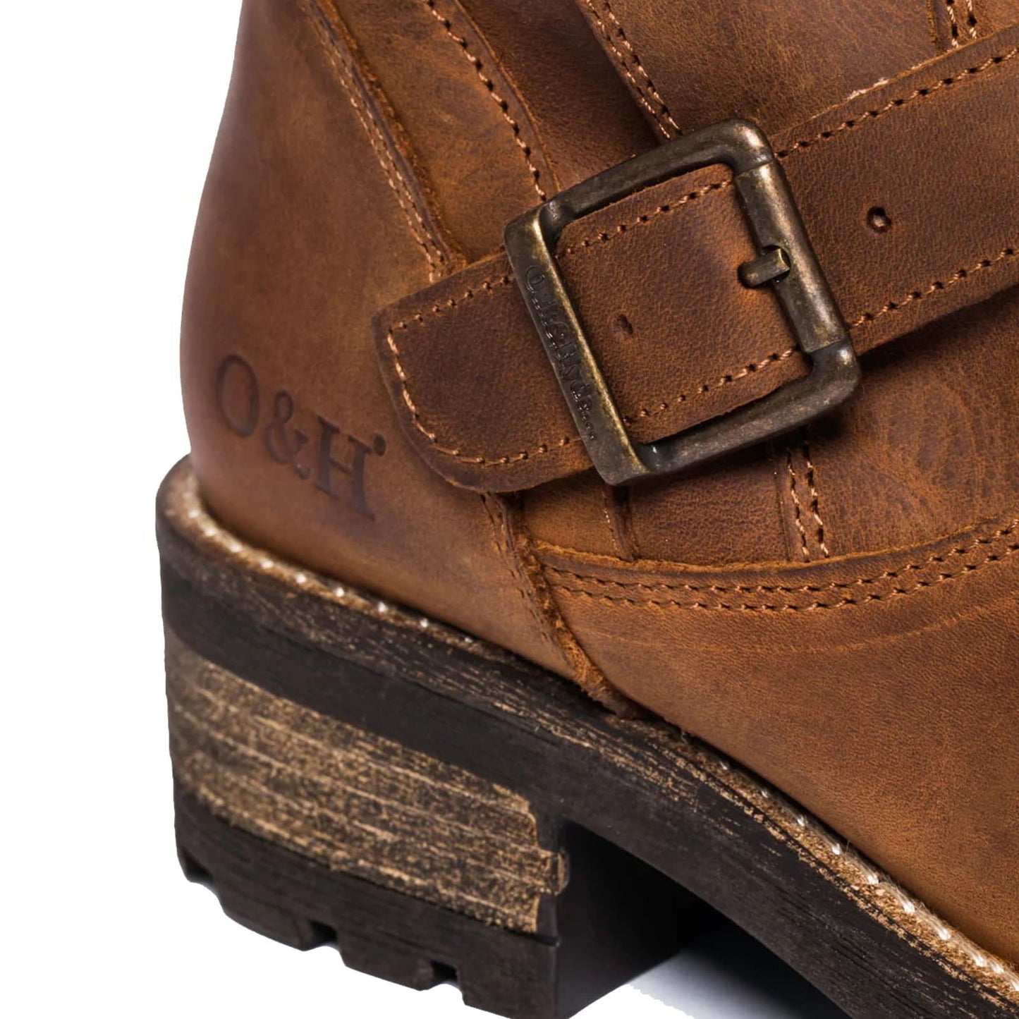Close-up of a brown leather boot with an ankle strap and a bronze buckle. The brand "O&H" is stamped on the side of the boot.