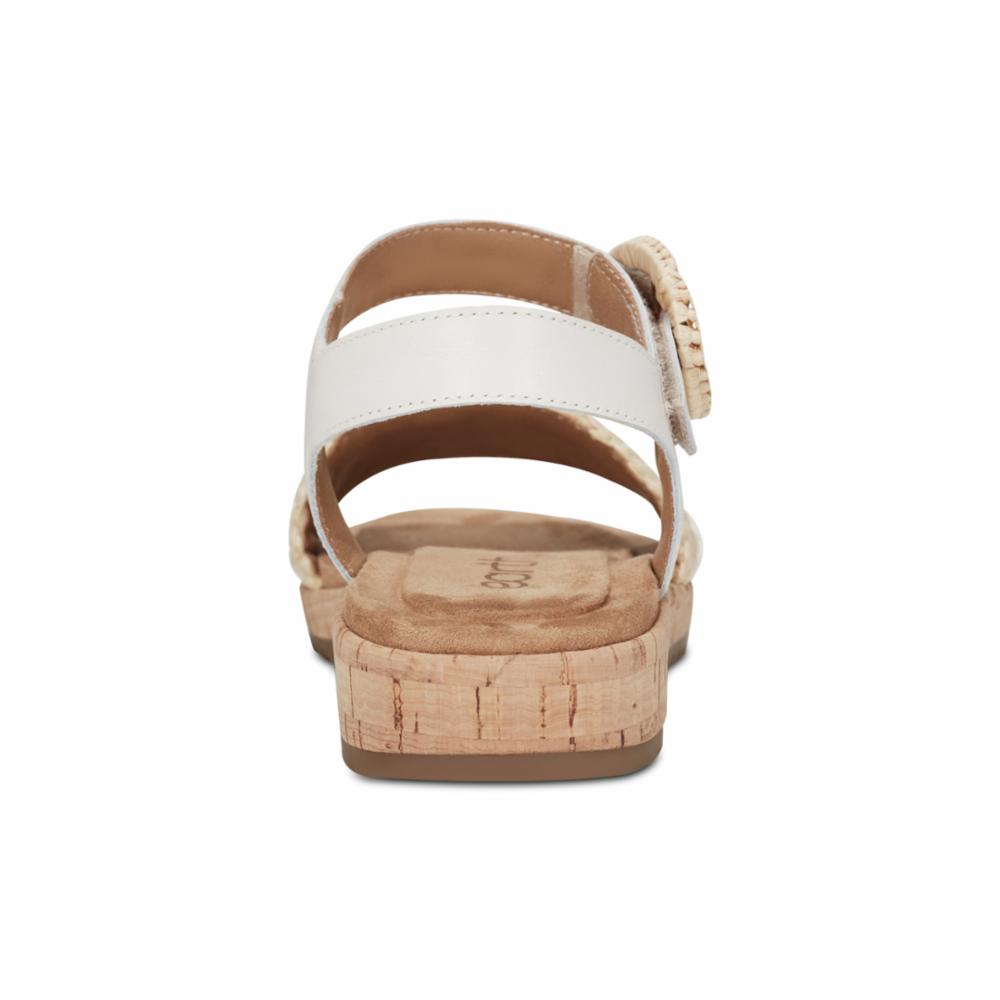 White sandal with adjustable ankle strap, cork sole, and round rattan-style buckle.