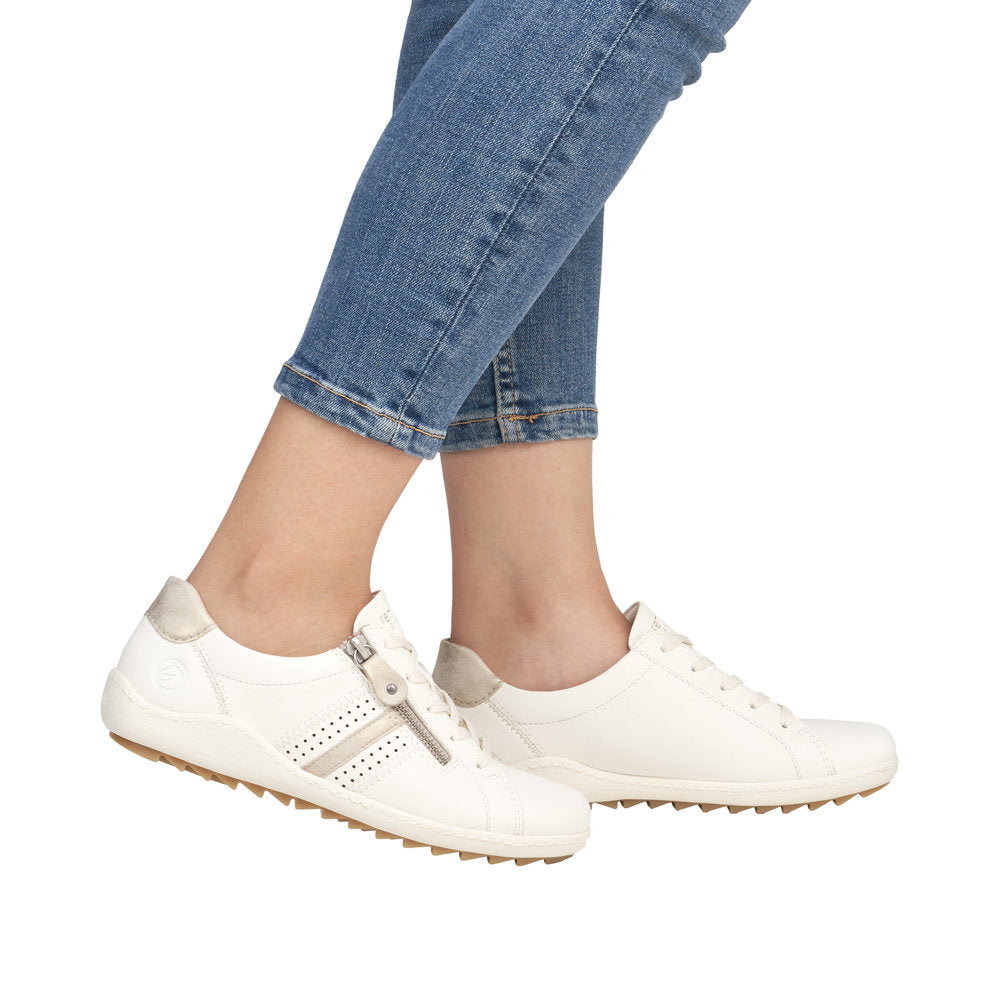 A person wearing white leather sneakers with side zippers.