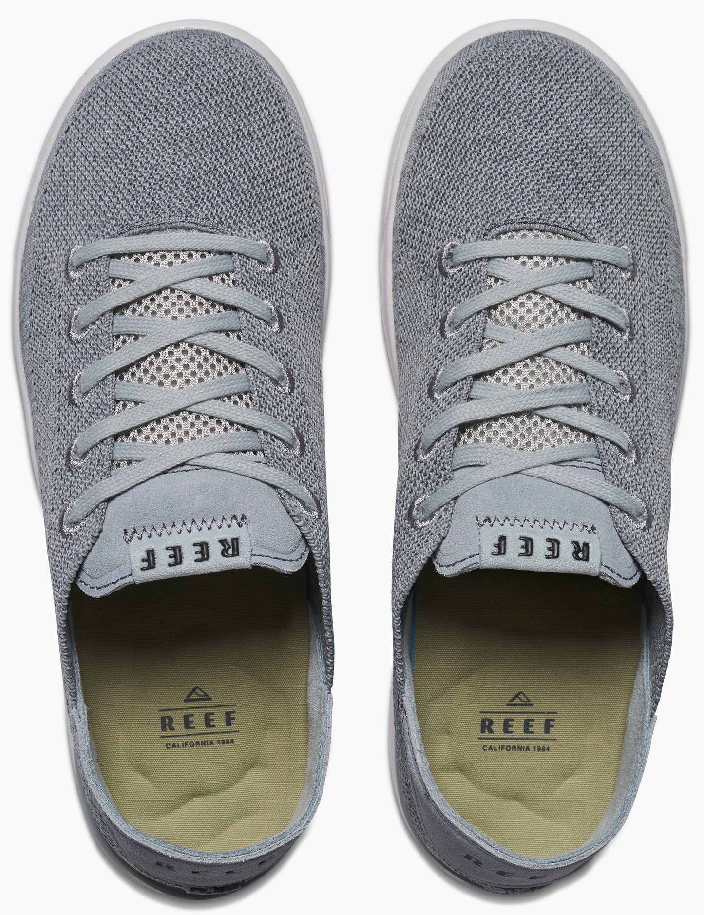 Overhead shot of two gray casual shoes with white laces, white rubber soles, and a light-brown insole with the text "REEF" visible.