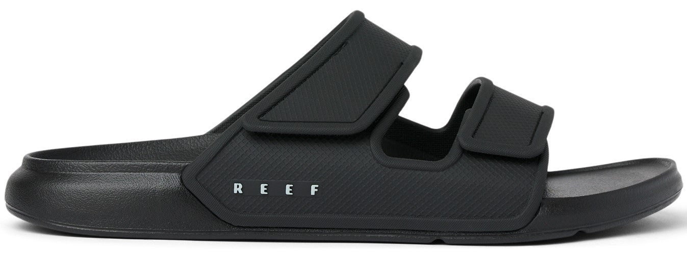 A black slide sandal with two adjustable straps and the word REEF printed on the side.