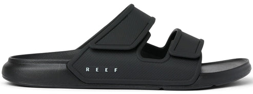A black slide sandal with two adjustable straps and the word REEF printed on the side.