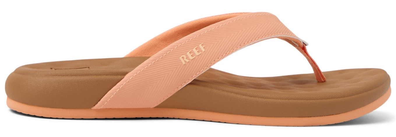 A peach-colored sandal with REEF printed on the strap and a brown sole.