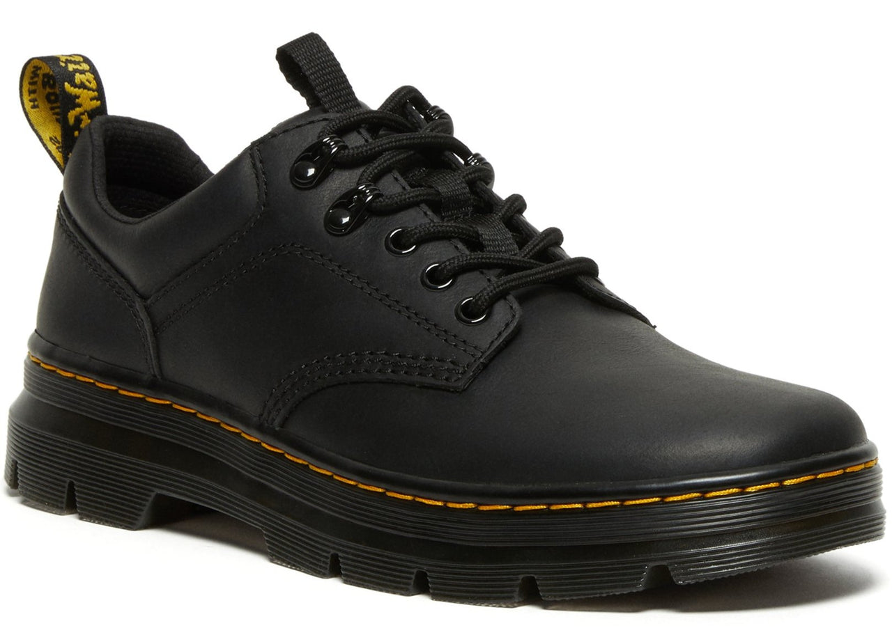 A black leather, low-top shoe with black laces, black eyelets, a pull tab on the heel with yellow text, and a thick, layered black sole with yellow stitching.